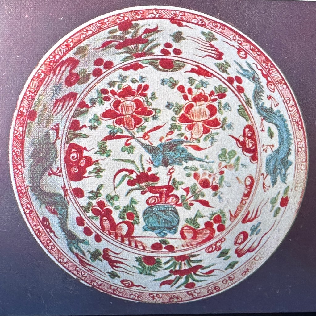 一個圓形的陶瓷盤，中央有多種花卉和動物圖案，顏色以紅色和藍色為主，外圍有細緻的裝飾邊緣。